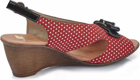Red and white polka dot sandal with black straps and decorative flower on wedge heel.