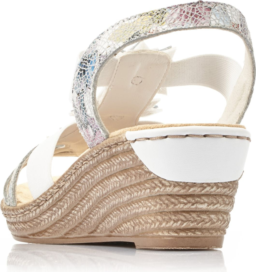 Wedge sandal with white straps, decorated with a flower, and an elastic ankle strap with a colorful pattern.
