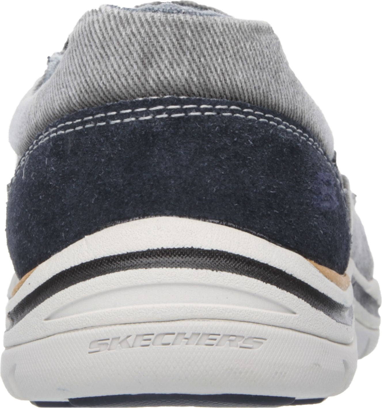 Close-up view of the back of a slip-on shoe, featuring a denim heel collar, a dark blue suede heel, and a white midsole with black and tan accents. The brand name "SKECHERS" is embossed on the midsole.