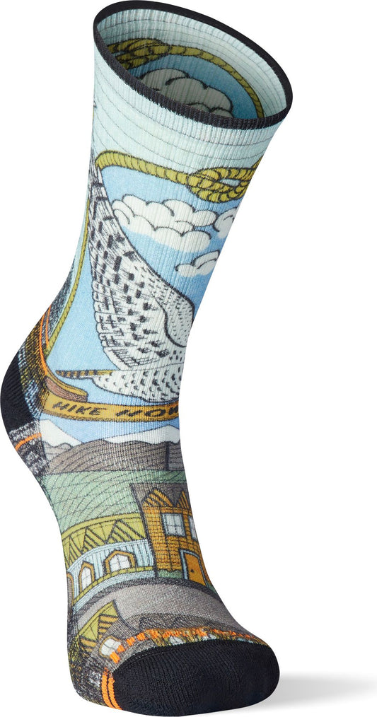 A patterned sock with a light blue top band, featuring a drawing of an owl, clouds, "HIKE MORE" text, and buildings.