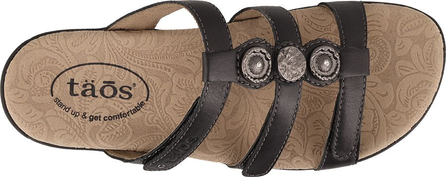 A sandal with black straps and three silver round decorative medallions.