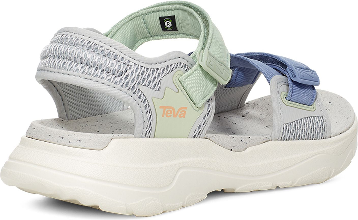 A sandal with a white and gray sole, light gray mesh accents, and light green and blue velcro straps. 'TEVA' in salmon color is printed on the side.
