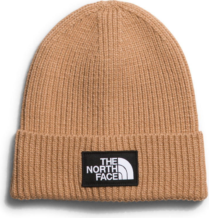 Ribbed-knit tan beanie with a black rectangular patch that reads "THE NORTH FACE" and a white half-dome logo.