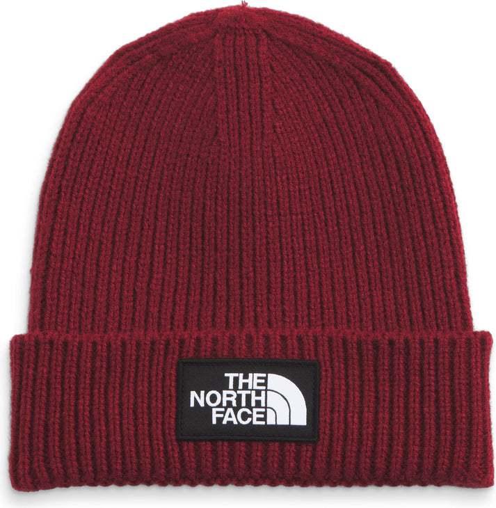 Red ribbed beanie with a black patch containing white text and a half circle shape.