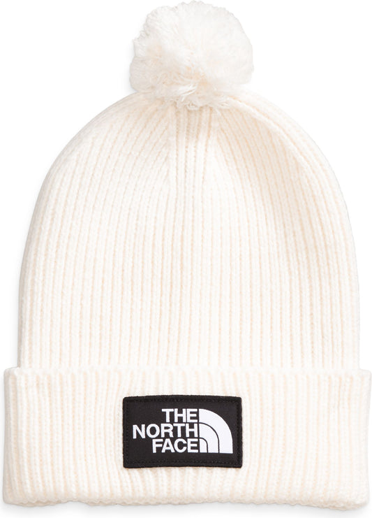 White ribbed knit beanie hat with pompom and a black patch with the white words "THE NORTH FACE" and a white half-circle.