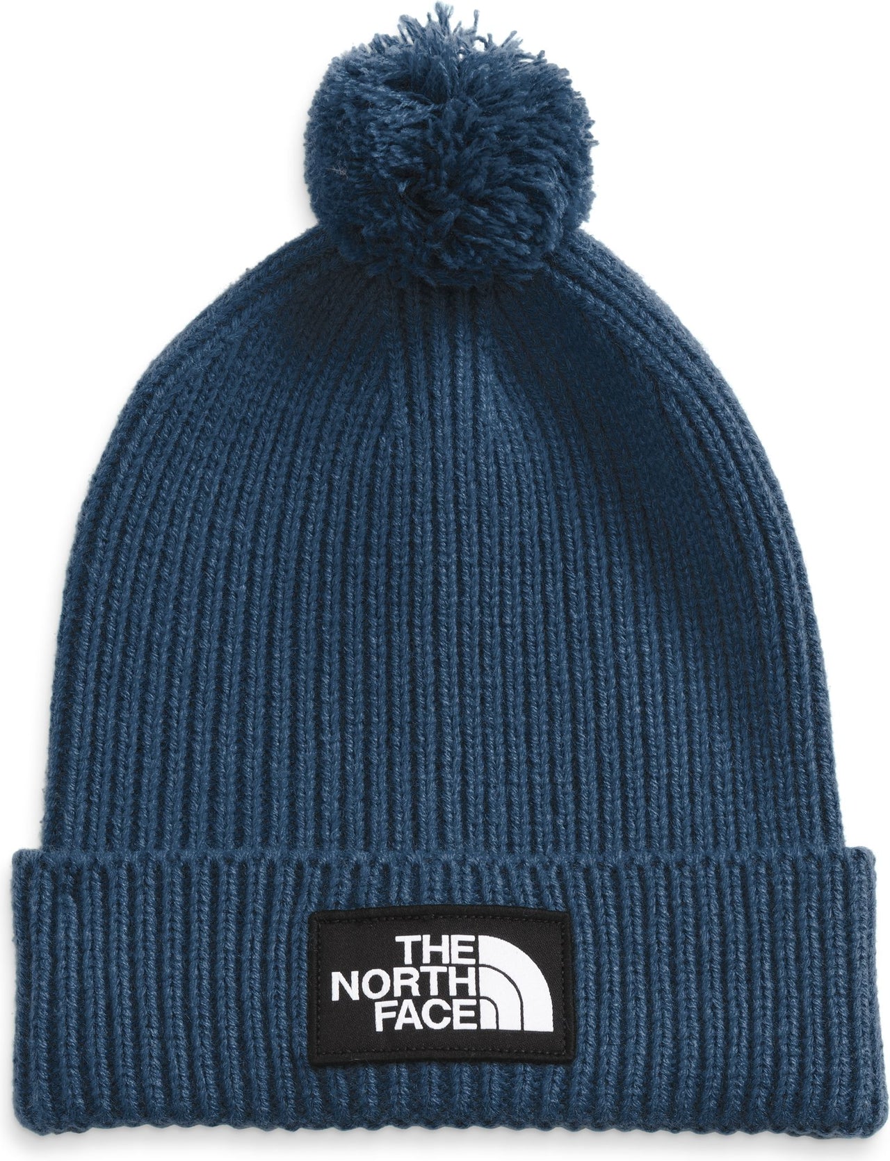 Close-up of a blue knit beanie with a pompom and a black patch with the words "THE NORTH FACE" written in white.