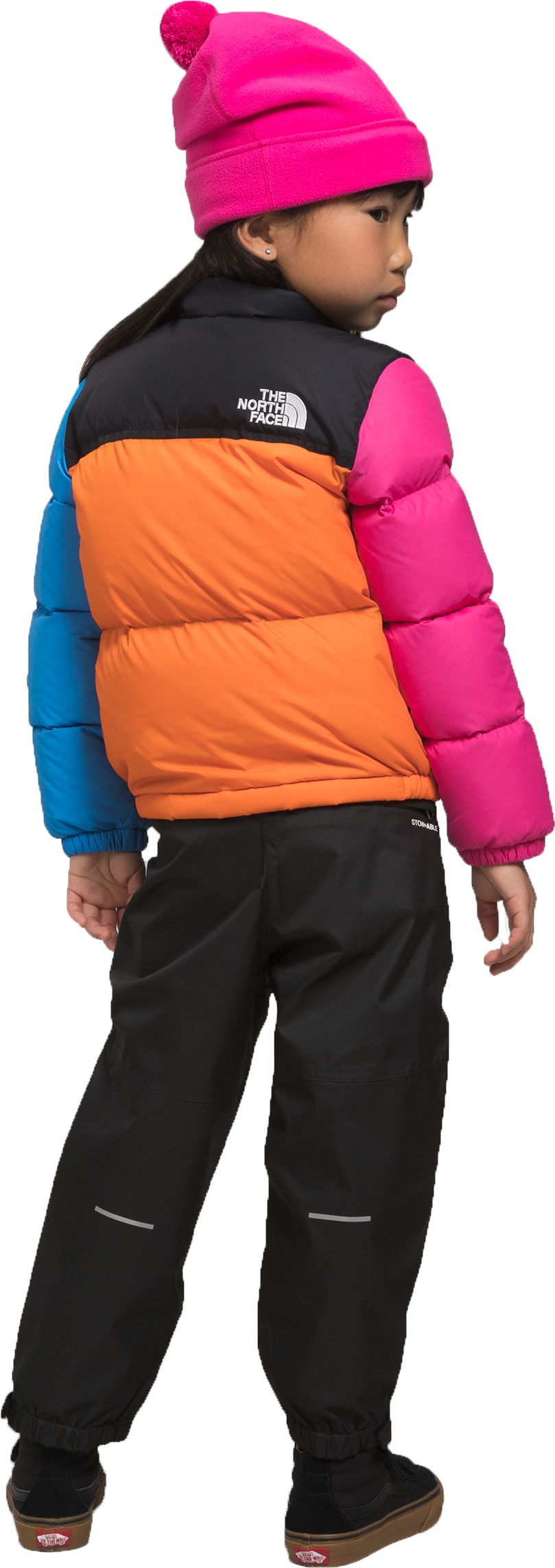 A child with a bright pink hat, wearing a colorful puffy jacket with black pants.