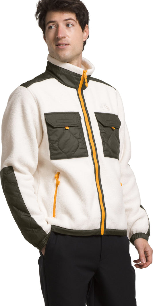 A man wears a cream fleece jacket with an olive green chest and shoulder yoke, two olive green chest pockets and an orange zipper.