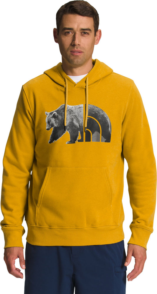 A man wearing a yellow hoodie with a bear and mountain logo on the front.