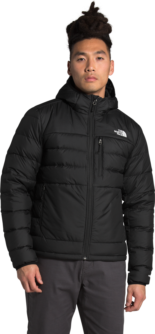 A man wears a black hooded puffer jacket with a zipper.