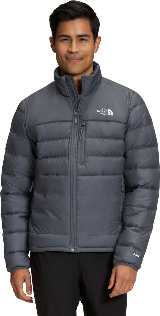 A man wearing a gray puffer jacket with a zipper and the logo on the upper right.