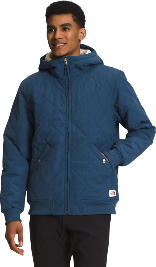 A person wearing a quilted blue hooded jacket and black pants.