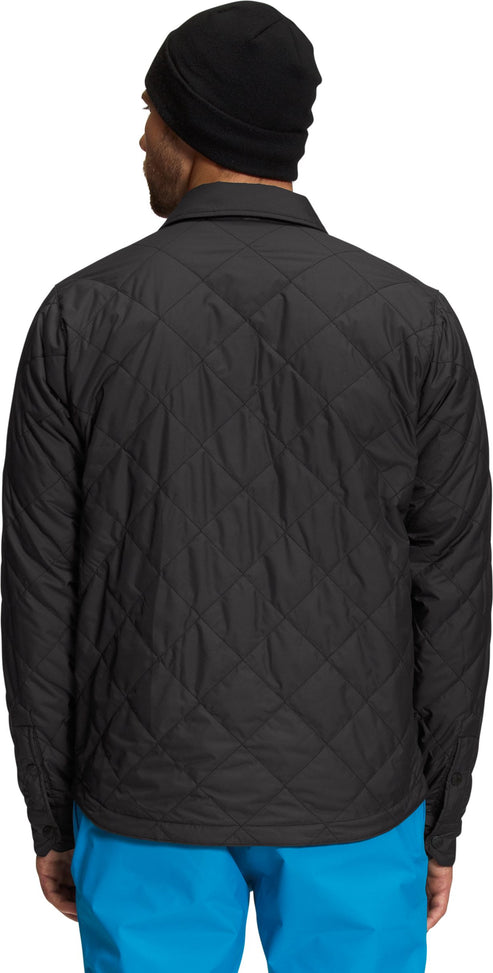 Back view of a man wearing a black quilted button down jacket with a black beanie and blue pants.