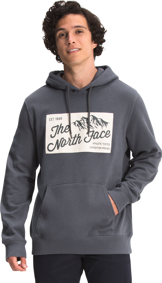Man wearing a gray pullover hoodie with a white logo graphic of mountains and text that reads "The North Face, Est. 1966, Athlete Tested Expedition Proven".
