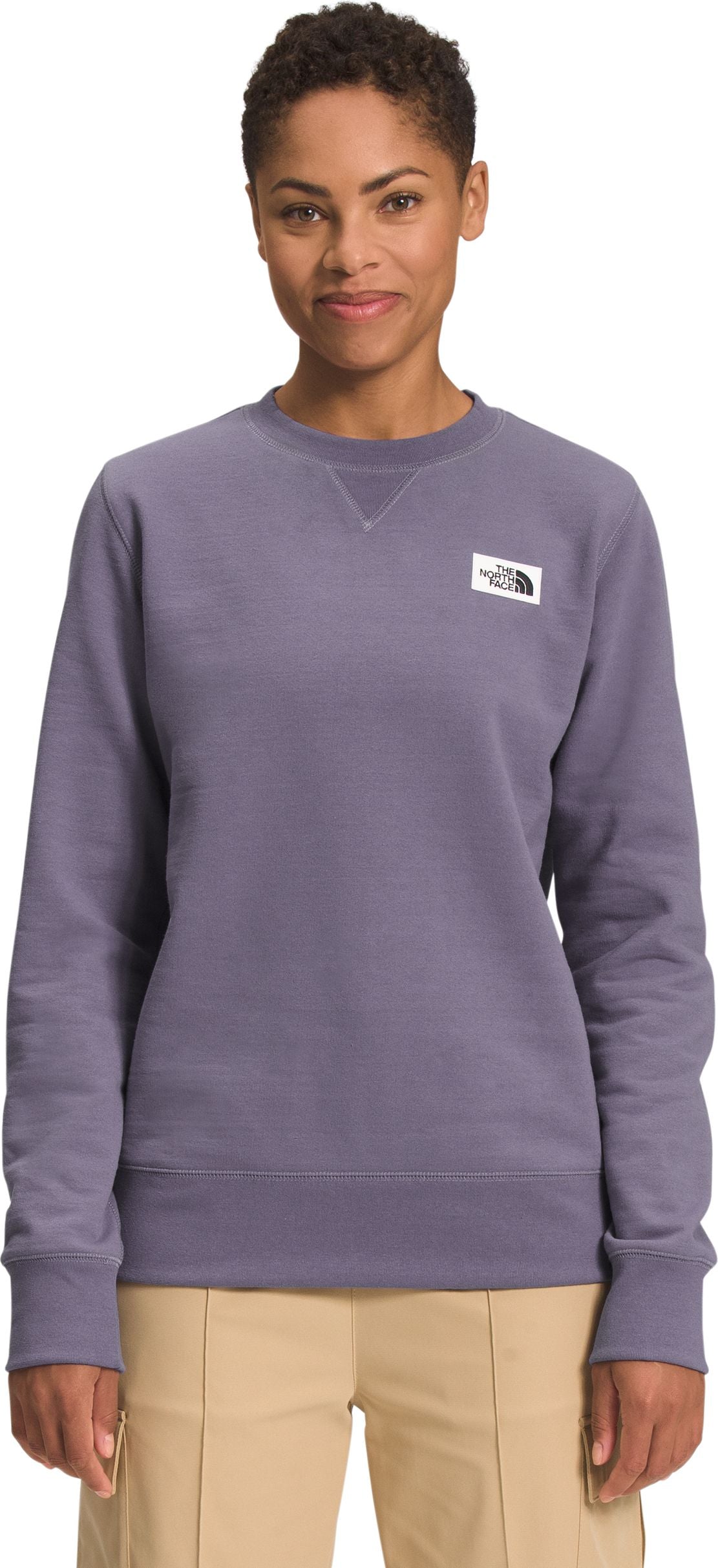 A woman wears a long-sleeved, light-purple sweatshirt with a white square label on the upper-left of the chest.