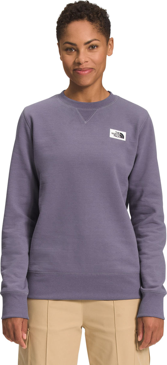A woman wears a long-sleeved, light-purple sweatshirt with a white square label on the upper-left of the chest.