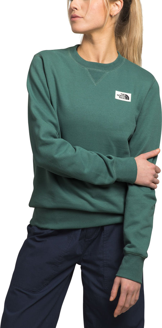 Woman wearing a green crew neck sweatshirt and blue pants.