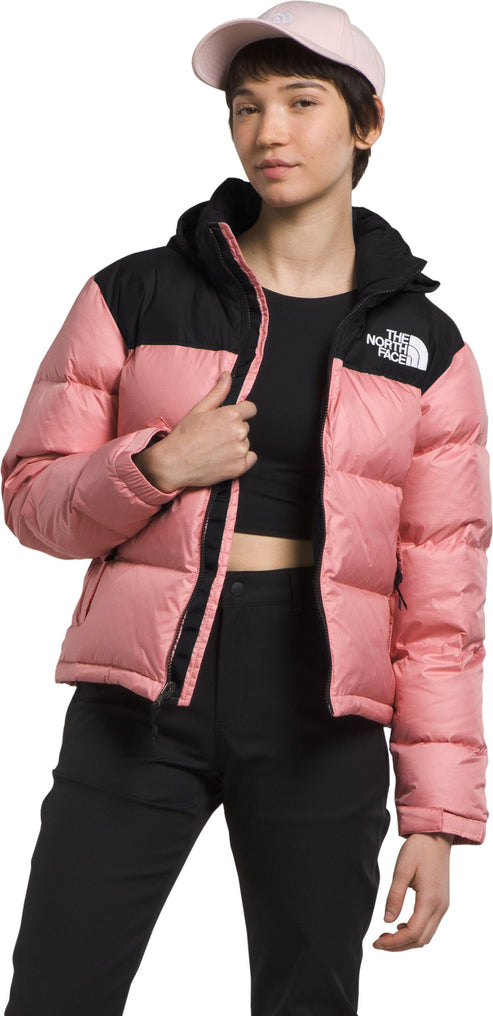 A woman wearing a pink baseball cap and a pink and black puffer jacket with black pants.