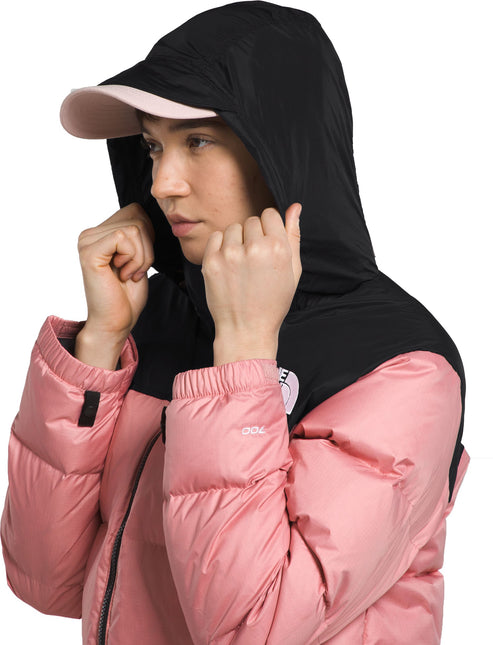 A woman wearing a color-blocked pink and black hooded down jacket, with a hat that has a pink brim.