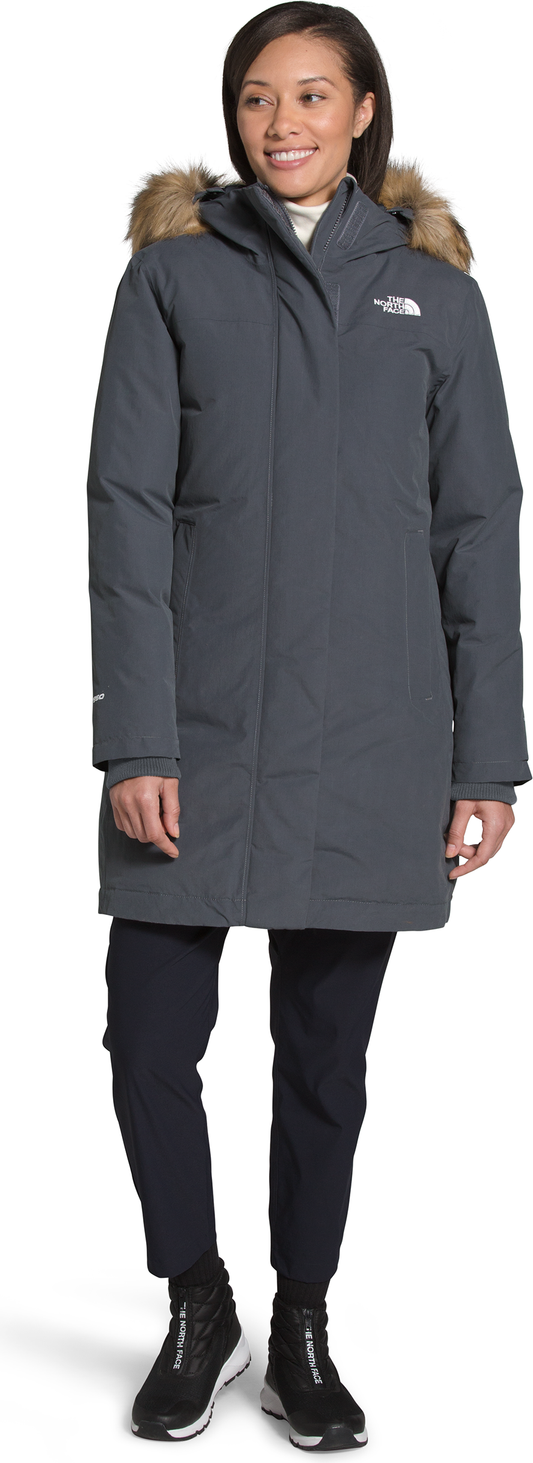 A person wearing a grey parka with fur trim, paired with black pants and shoes.
