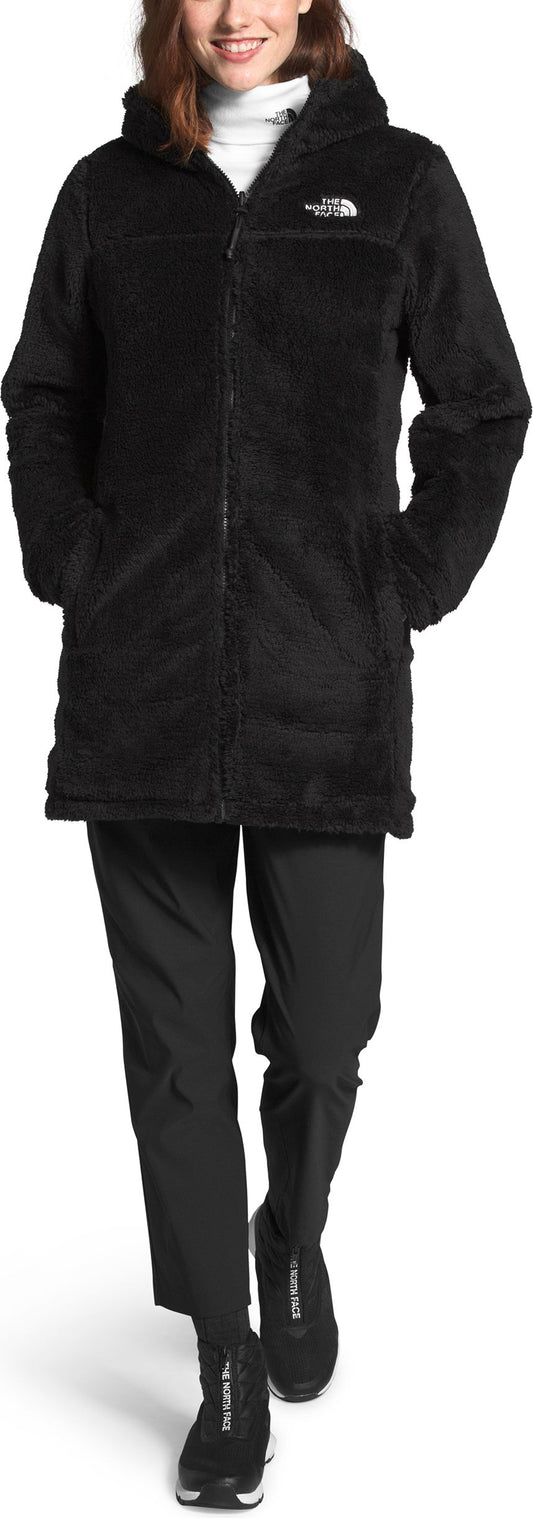 A woman in a black, hooded, zip-up jacket, black pants, and matching zip-up shoes.