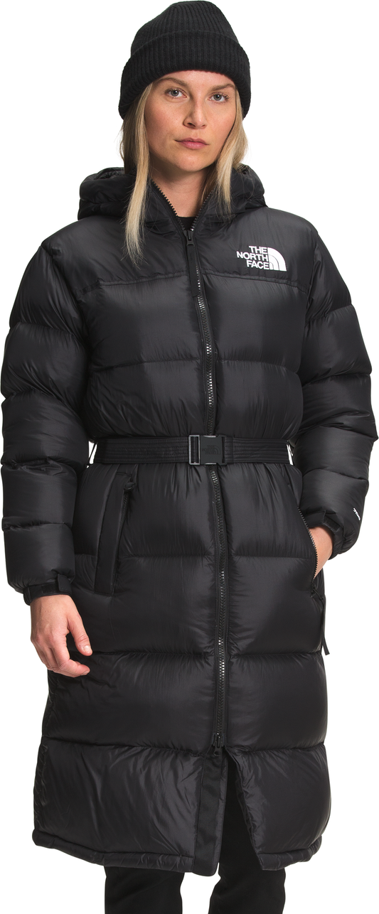 A woman wears a long black puffer coat with a matching belt and a black beanie.