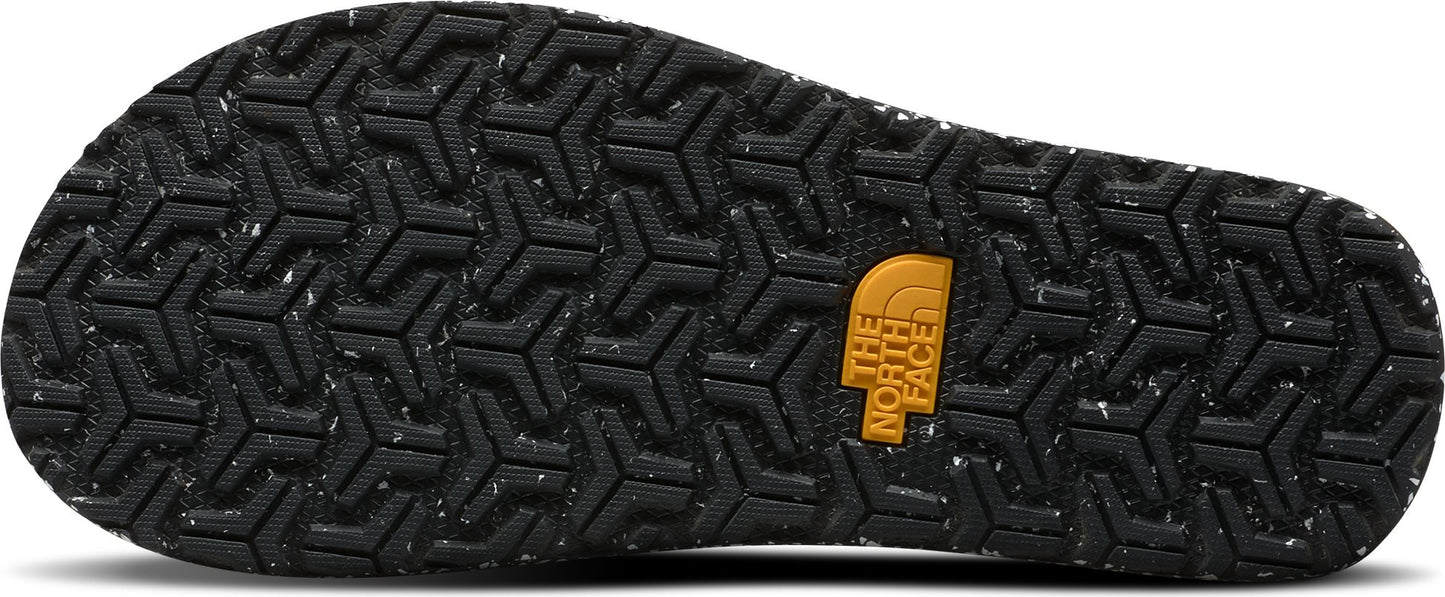 The textured black sole of a shoe with a repeating triangular pattern and a tan logo.