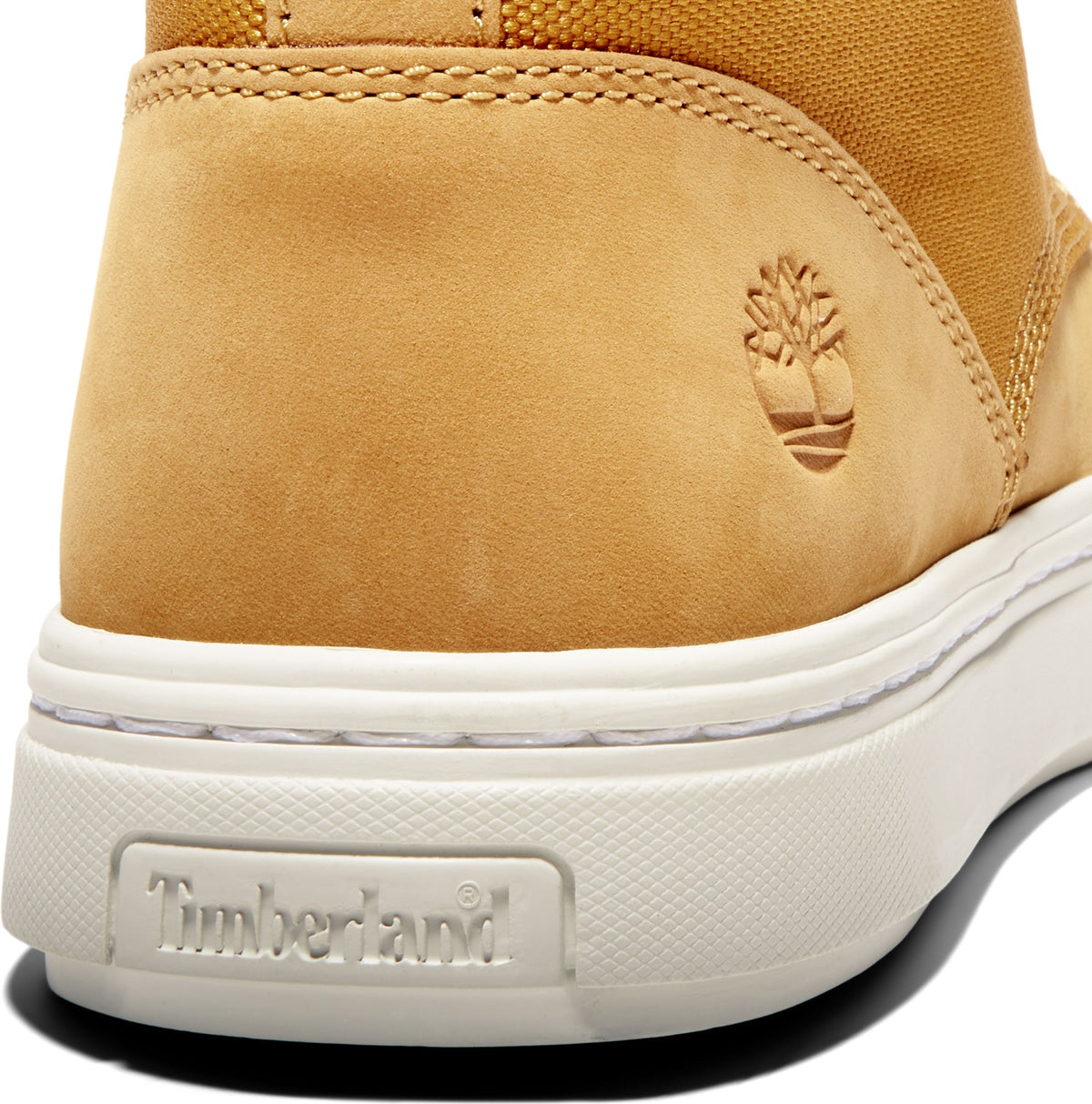 Close-up of a tan suede boot heel featuring the embossed logo, stacked on a white sole with the brand name embossed on the heel.