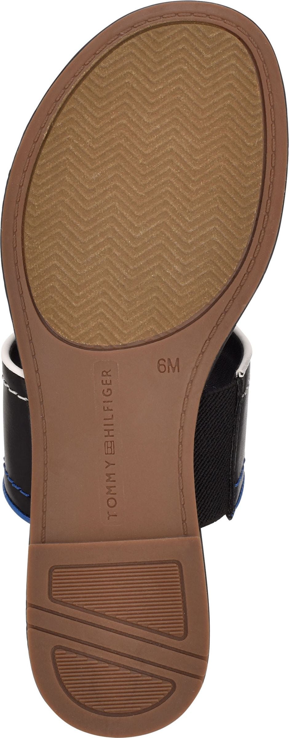 The bottom of a sandal showing the sole, which is tan and has a chevron pattern. The inner part of the sole has TOMMY HILFIGER and 6M printed on it.