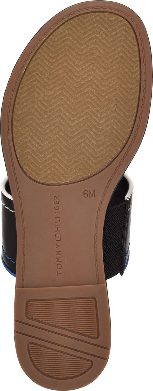The bottom of a sandal showing the sole, which is tan and has a chevron pattern. The inner part of the sole has TOMMY HILFIGER and 6M printed on it.