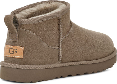 Rear view of a short, taupe-colored suede boot with plush lining and a logo on the side.