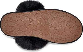 Close-up of the sole of a black, furry slipper. The brown rubber sole has a pattern of interconnected UGG logos.