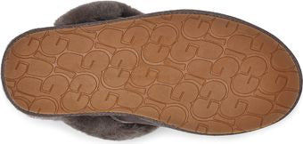 A slipper with a brown rubber sole with the letters UGG on it.