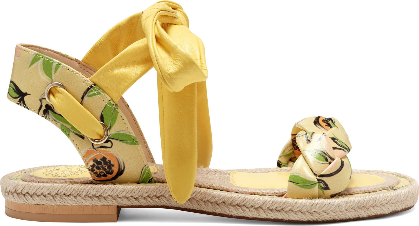 Flat sandal with a jute-style sole and yellow straps with fruit print, one tied around the ankle.