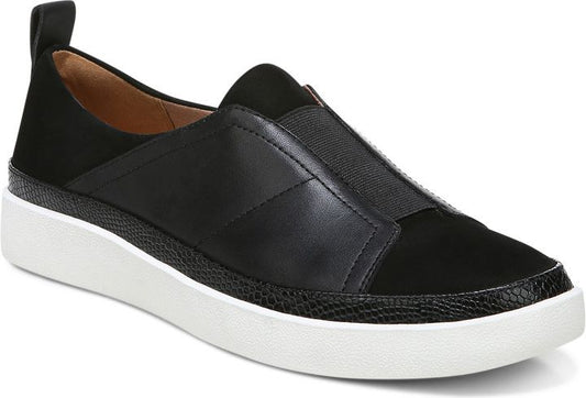 A black slip-on shoe with an elastic band, leather and suede panels, a textured band between the upper and the white sole, and a pull tab at the back.